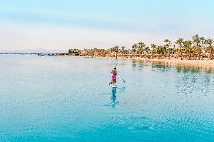 Ein Mann steht auf einem Paddleboard und gleitet über das ruhige Wasser des Roten Meeres.