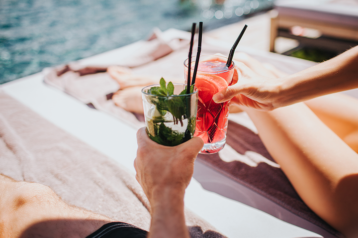 Ein Paar genießt Cocktails am Strand, umgeben von Sand und Wellen, während die Sonne untergeht.