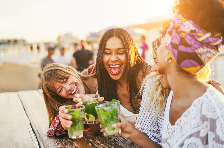 Vier Freundinnen stoßen mit Cocktails an und feiern ausgelassen auf einer Strandparty