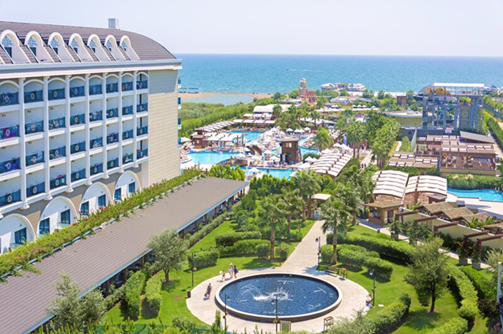 Hotelanlage mit einem erfrischenden Pool, einer weitläufigen Rasenfläche und dem Strand im Hintergrund, ideal für entspannte Tage im Freien.
