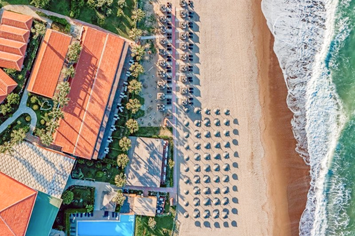Luftaufnahme eines Strandes mit einem Resort-Hotel, das in die Küstenlandschaft eingebettet ist.