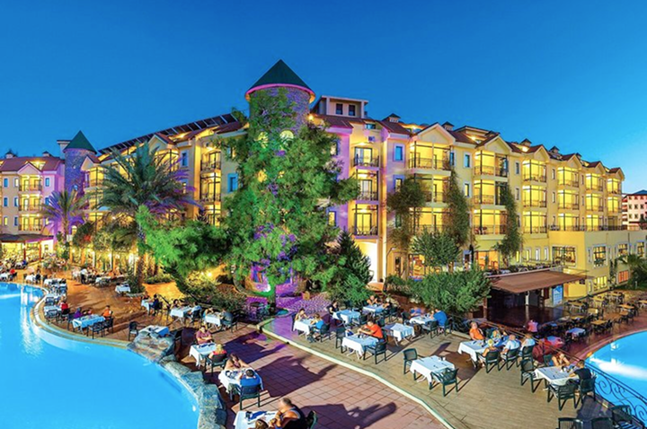 Nachtansicht eines Hotels mit einem glitzernden Pool und einer einladenden Patiofläche, die romantisch beleuchtet ist.
