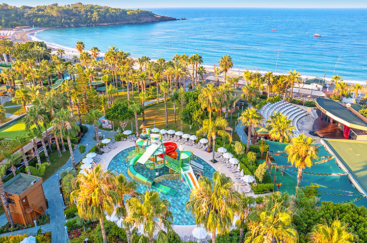 Luftaufnahme des Strandes und Resorts mit Wasserrutschen, die lebhafte Farben und entspannte Urlaubsatmosphäre zeigen.