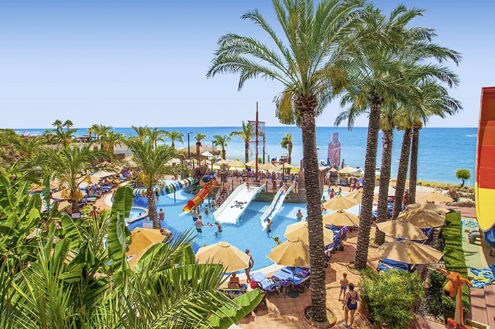 Weitläufiger Pool mit Palmen und einer bunten Wasserrutsche für Spaß und Entspannung.