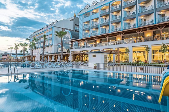 Hotelgebäude mit mehreren Balkonen und beleuchtetem Pool im Vordergrund.