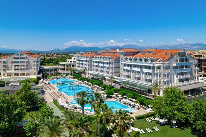 Große Hotelanlage mit mehreren mehrstöckigen Gebäuden, mehreren Pools und Liegen, umgeben von Palmen und Bergen im Hintergrund.
