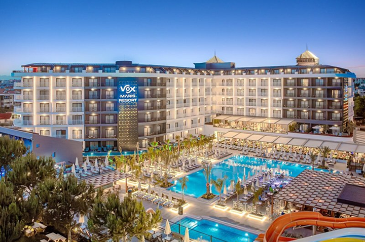 Großes mehrstöckiges Hotel mit beleuchtetem Schriftzug und mehreren Pools mit Liegen und Sonnenschirmen davor. Großes mehrstöckiges Hotel mit beleuchtetem Schriftzug und mehreren Pools mit Liegen und Sonnenschirmen davor.