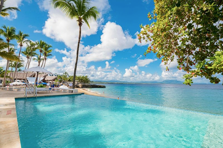 Blick auf den Pool des Resorts, umgeben von tropischer Vegetation, einladenden Liegen und Meerblick
