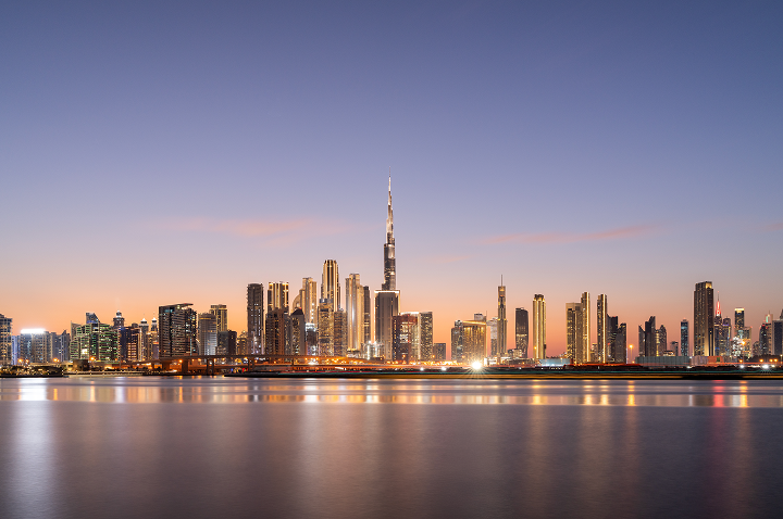 Die Skyline von Dubai bei Dämmerung, mit leuchtenden Wolkenkratzern und einem sanften, orangefarbenen Himmel.