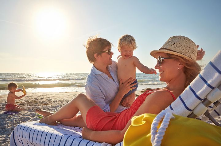 Eine Familie genießt einen sonnigen Tag am Strand, während ein Kind im Sand spielt.