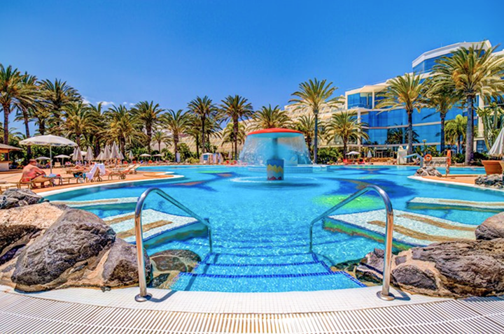 Ein Hotelpool mit einem Wasserfall und Palmen, ideal für Entspannung und Erholung in tropischer Atmosphäre.