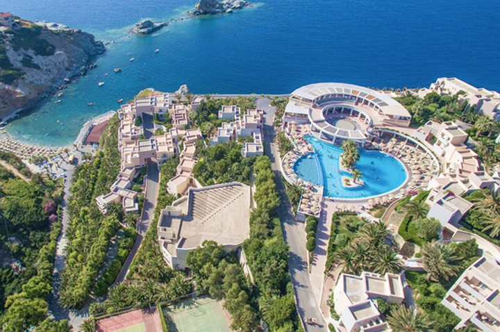 Aerialansicht des Hotels mit glitzerndem Pool, umgeben von Palmen und einem einladenden Erholungsbereich.