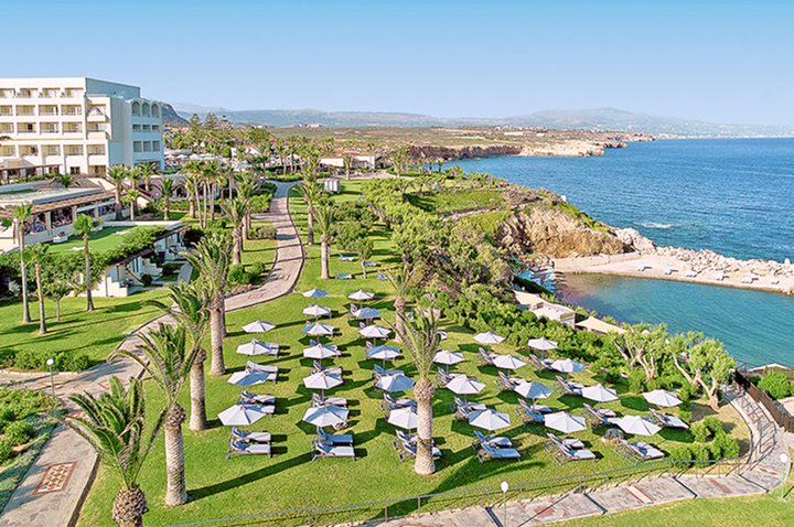 Luxuriöses Hotel mit grünen Wiesen und Sonnenschirmen, direkt am Meer gelegen.