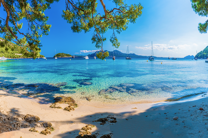 Ein sonniger Sandstrand mit klarem Wasser und mehreren Booten, die sanft an der Küste schaukeln.
