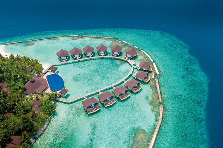 Blick von oben auf ein Resort mit Malediven-Bungalows auf einer Insel, umgeben von strahlend blauem Wasser und Palmen.