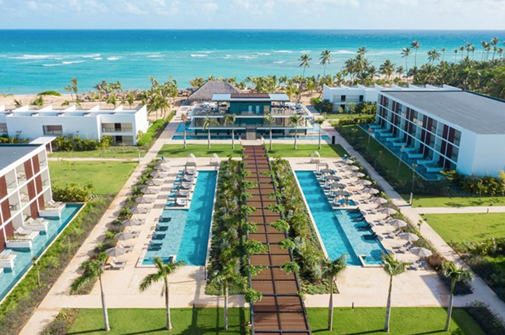 Blick auf ein Resort mit zwei langen Pools, Liegestühlen, Palmen und dem Meer im Hintergrund. Blick auf ein Resort mit zwei langen Pools, Liegestühlen, Palmen und dem Meer im Hintergrund.