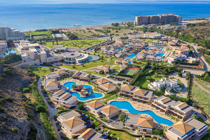 Luftaufnahme einer weitläufigen Hotelanlage mit mehreren Pools, Gebäuden mit roten Dächern und Blick auf das Meer.