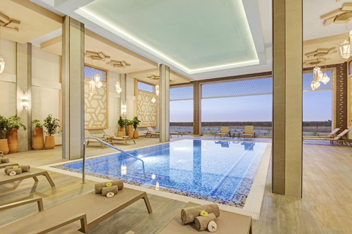 Innenraum eines modernen Hallenbads mit Liegen, Handtüchern und großen Fenstern mit Blick auf das Meer.