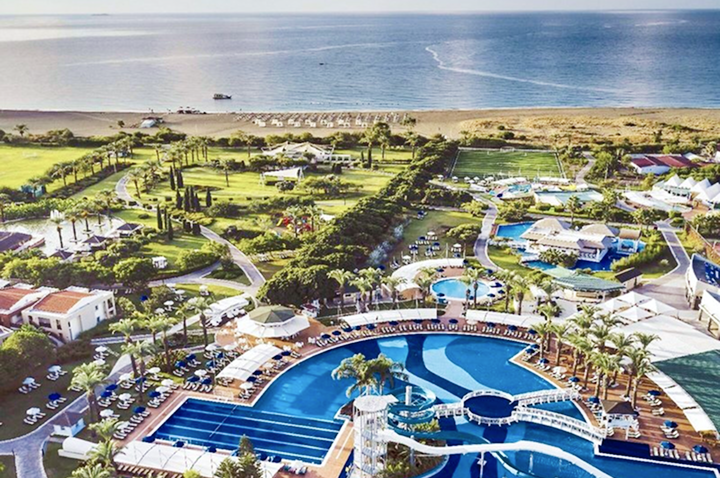 Luftaufnahme eines tropischen Resorts mit großen Schwimmbecken, Palmen, Liegestühlen und Strand am Meer.