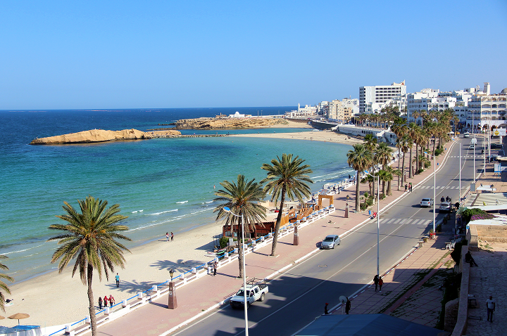 Blick auf einen Strand von Tunesien mit einer Stadt und einem großen Gewässer im Hintergrund