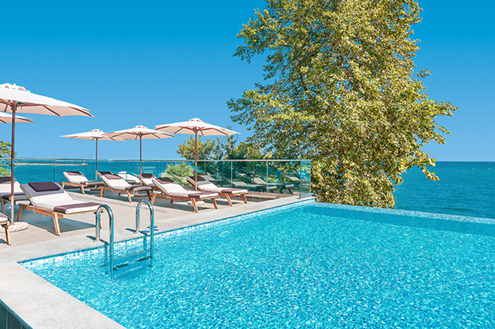 Ein Hotelpool mit Liegen und Sonnenschirmen, der einen herrlichen Blick auf den Ozean bietet.